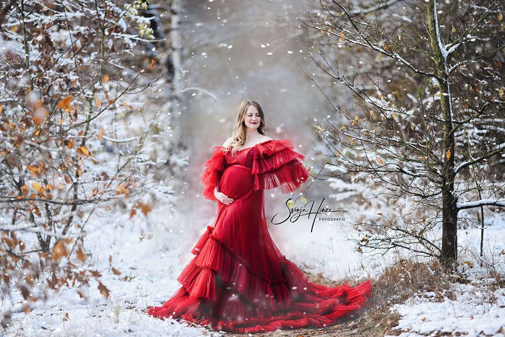 Eine schwangere Frau in einem roten Kleid steht im Schnee.