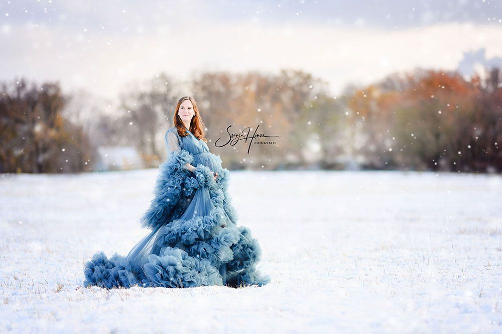 Eine schwangere Frau in einem blauen Kleid steht auf einem schneebedeckten Feld.