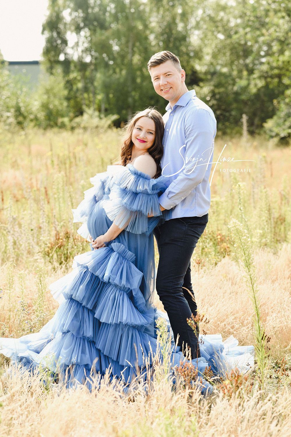 Eine schwangere Frau in einem blauen Kleid steht neben einem Mann auf einem Feld.