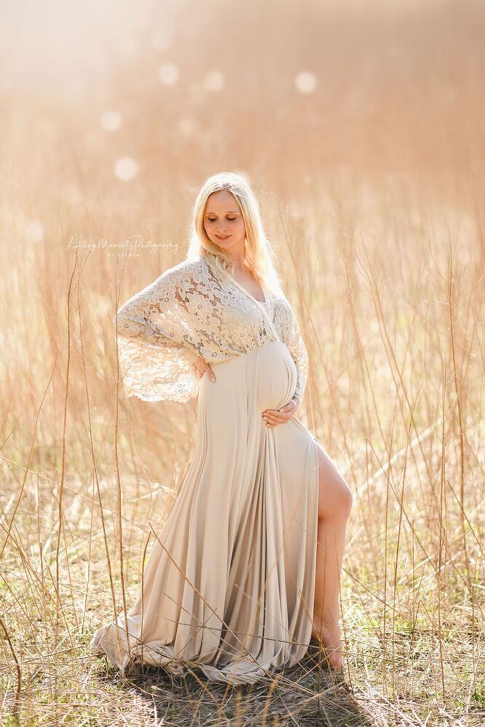 Eine schwangere Frau in einem langen weißen Kleid steht auf einem Feld.