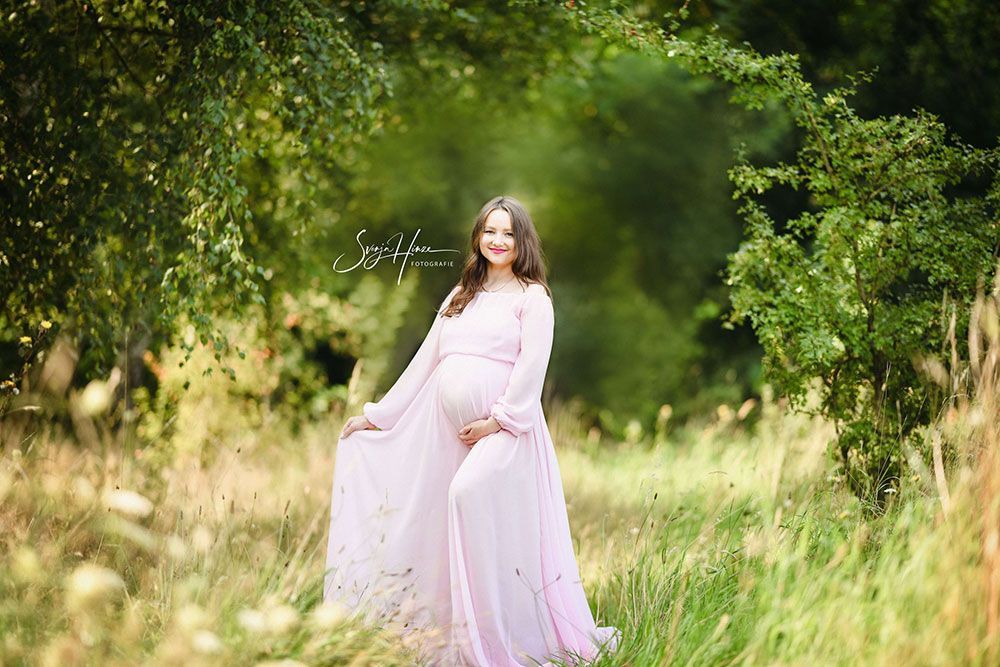 Eine schwangere Frau in einem rosa Kleid steht auf einem Feld.