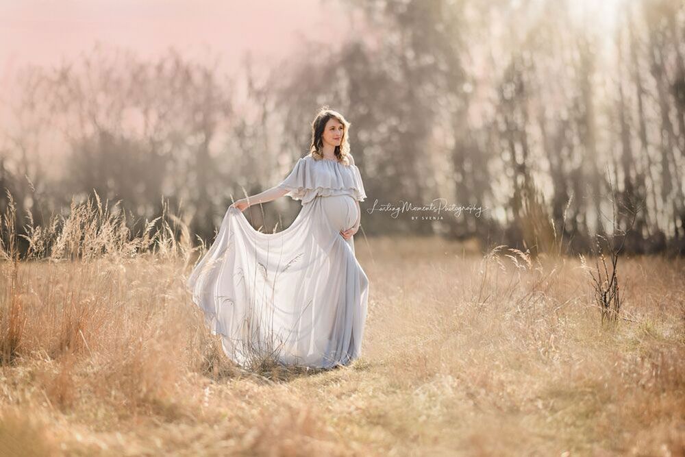 Eine schwangere Frau in einem weißen Kleid steht auf einem Feld.