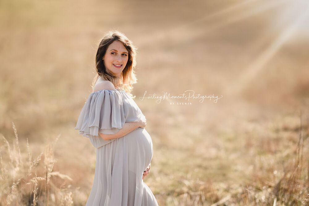 Eine schwangere Frau steht auf einem Feld und hält ihren Bauch.