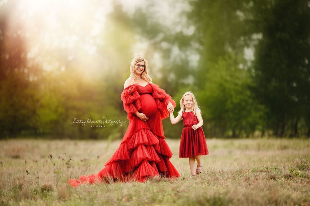 Eine schwangere Frau in einem roten Kleid steht neben einem kleinen Mädchen in einem roten Kleid.