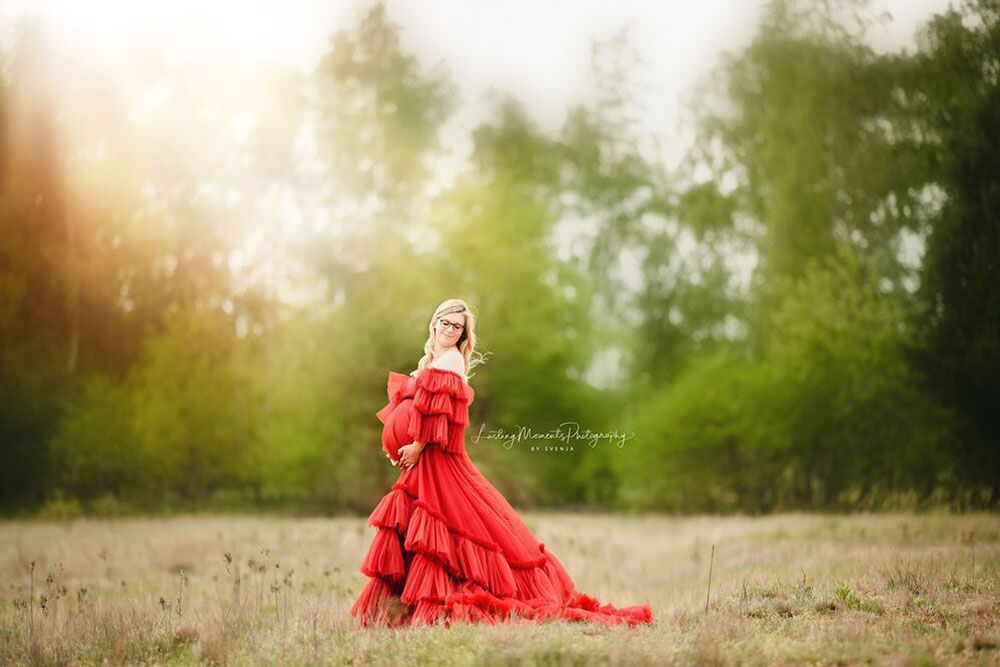 Eine schwangere Frau in einem roten Kleid steht auf einem Feld.