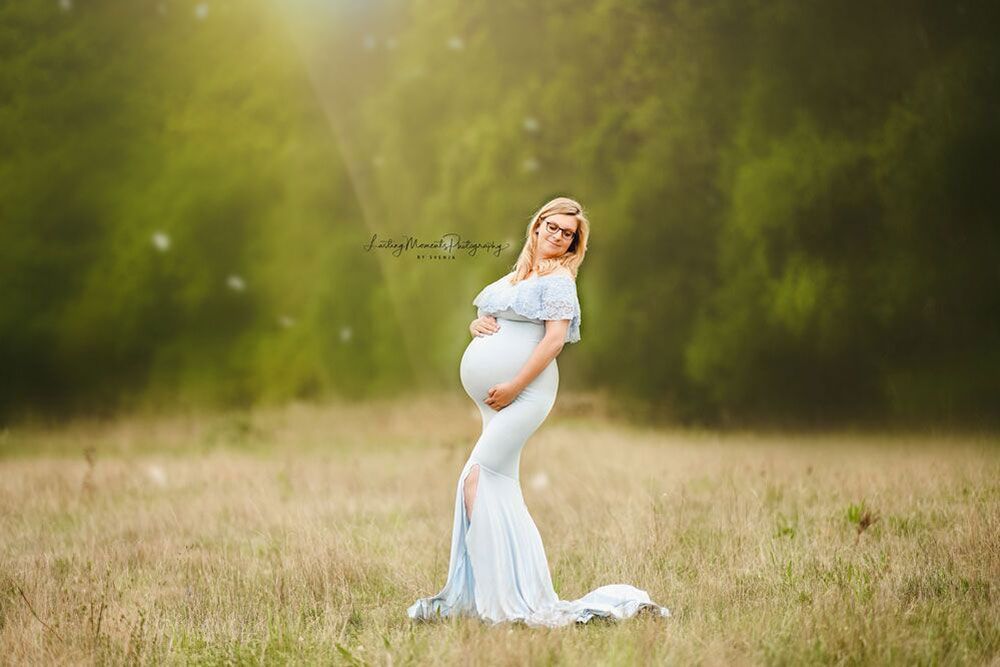 Eine schwangere Frau in einem weißen Kleid steht auf einem Feld.