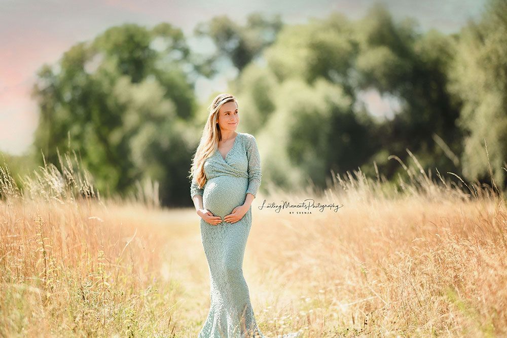 Eine schwangere Frau in einem blauen Kleid steht auf einem Feld.