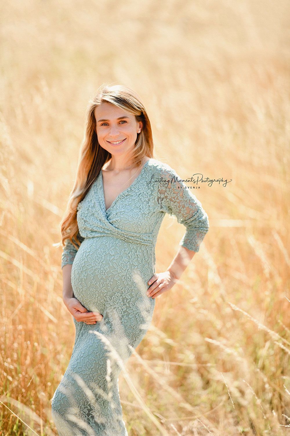 Eine schwangere Frau in einem grünen Kleid steht auf einem Feld mit hohem Gras.