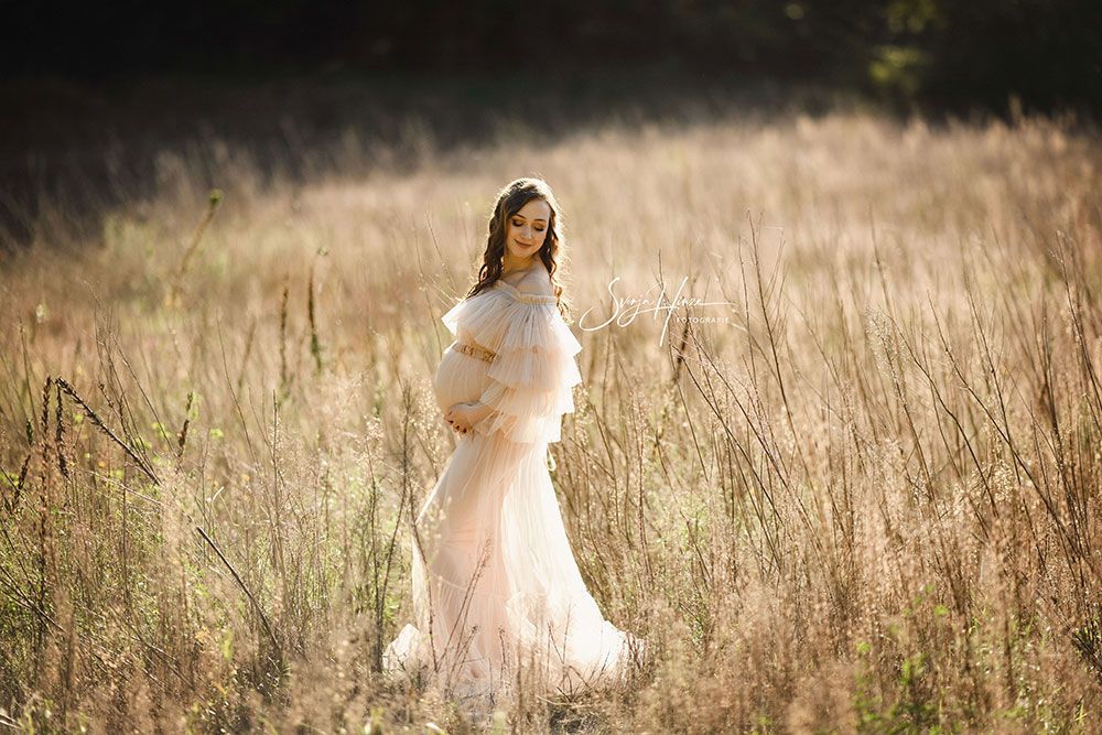 Eine schwangere Frau in einem weißen Kleid steht auf einem Feld.