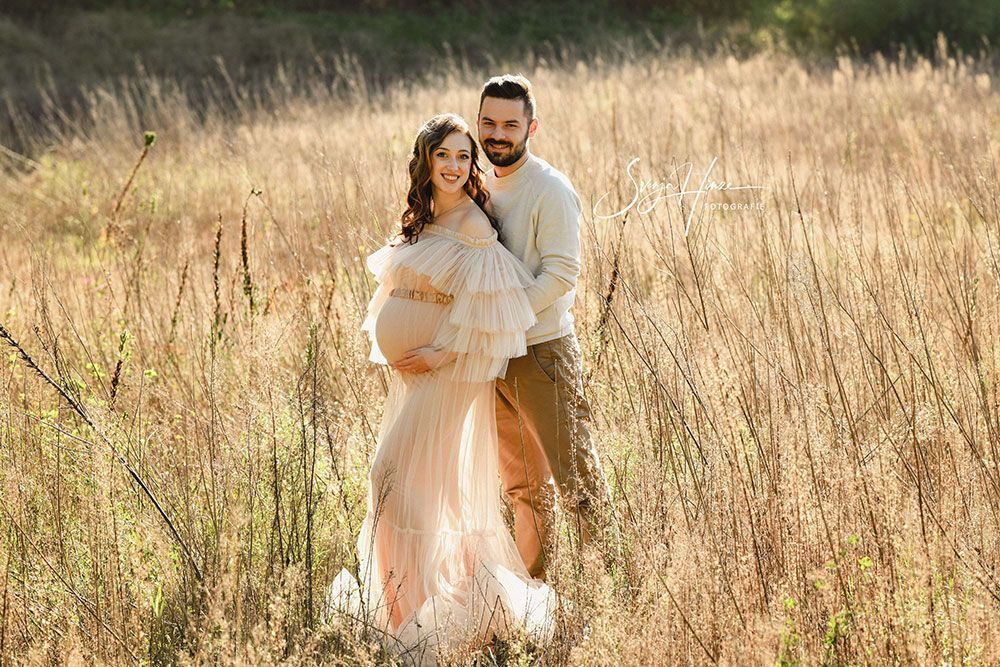 Eine schwangere Frau und ein Mann posieren auf einem Feld für ein Foto.
