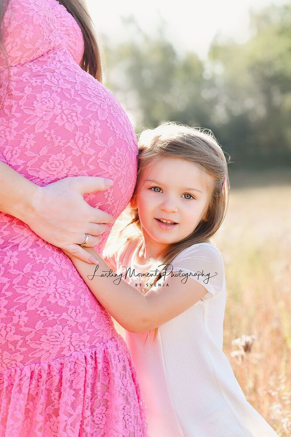 Ein kleines Mädchen umarmt den Bauch einer schwangeren Frau.