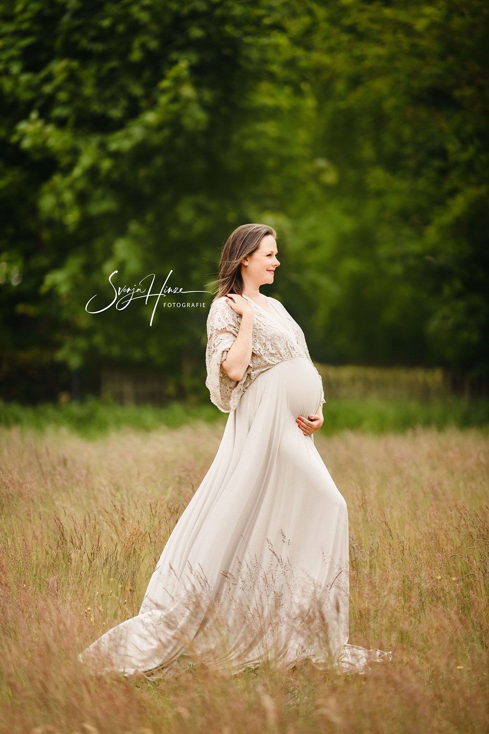 Eine schwangere Frau in einem weißen Kleid geht durch ein Feld.