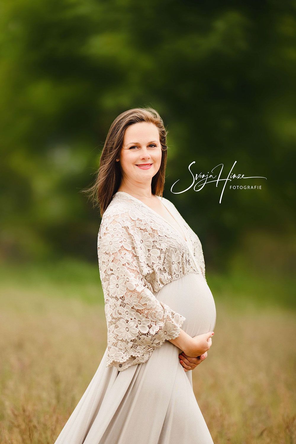 Eine schwangere Frau in einem weißen Kleid steht auf einem Feld und hält ihren Bauch.