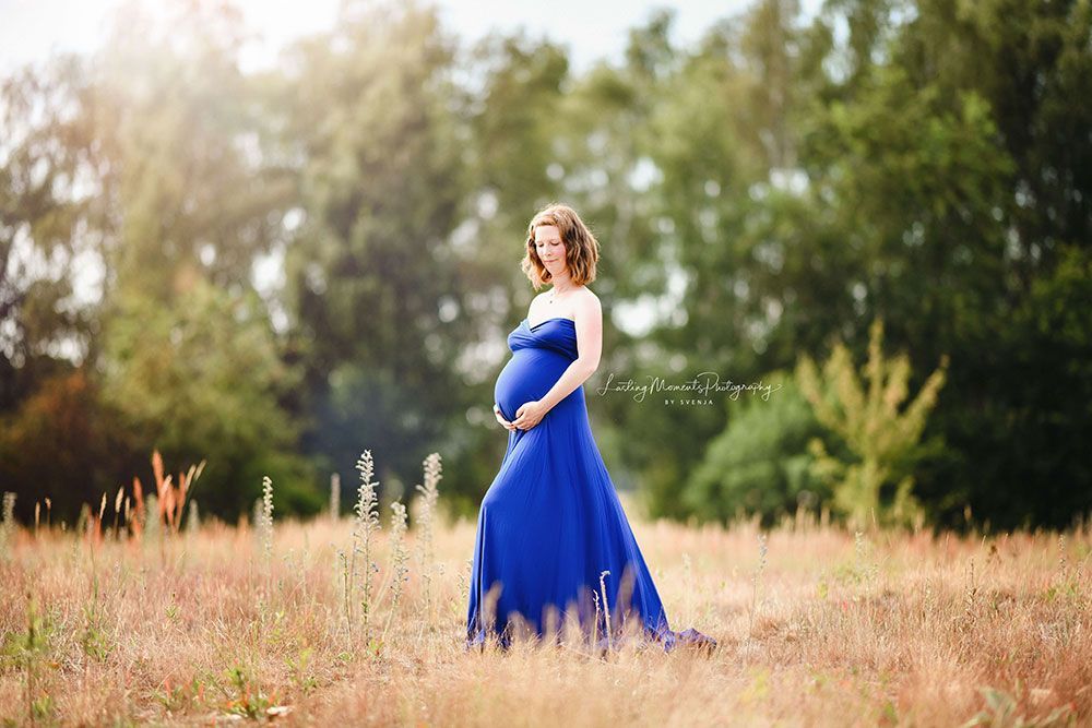 Eine schwangere Frau in einem blauen Kleid steht auf einem Feld.
