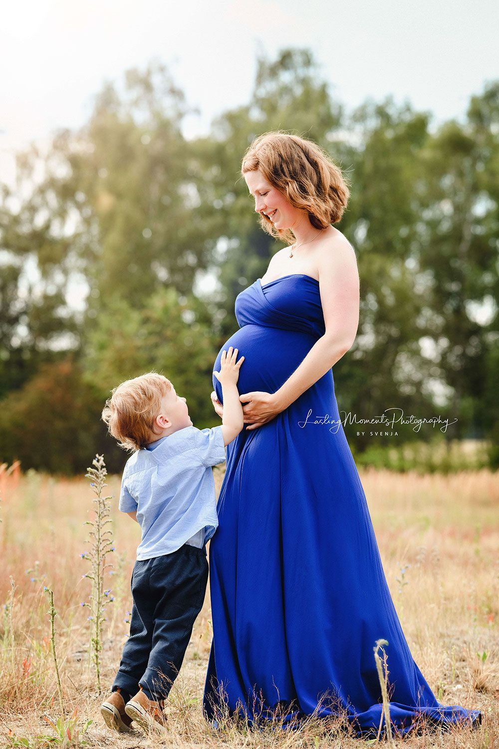 Eine schwangere Frau in einem blauen Kleid steht mit ihrem Sohn auf einem Feld.