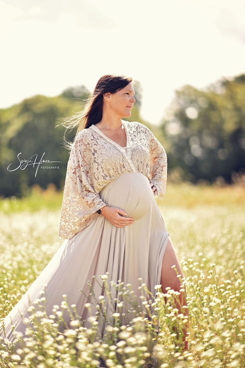 Eine schwangere Frau in einem weißen Kleid steht in einem Blumenfeld.