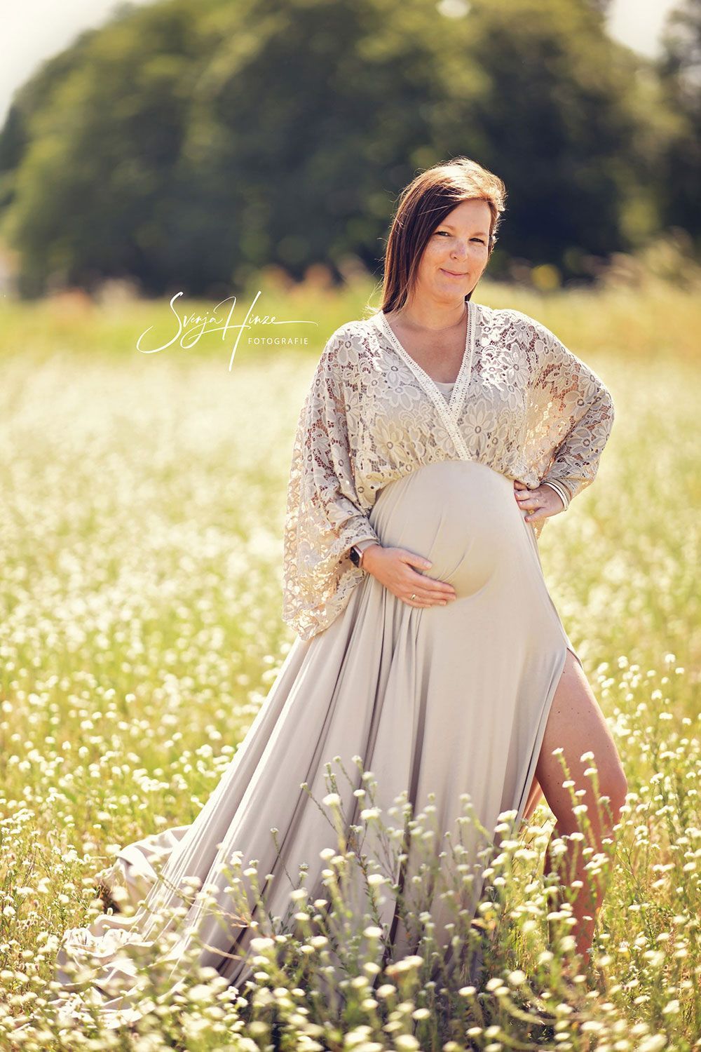 Eine schwangere Frau in einem weißen Kleid steht in einem Blumenfeld.