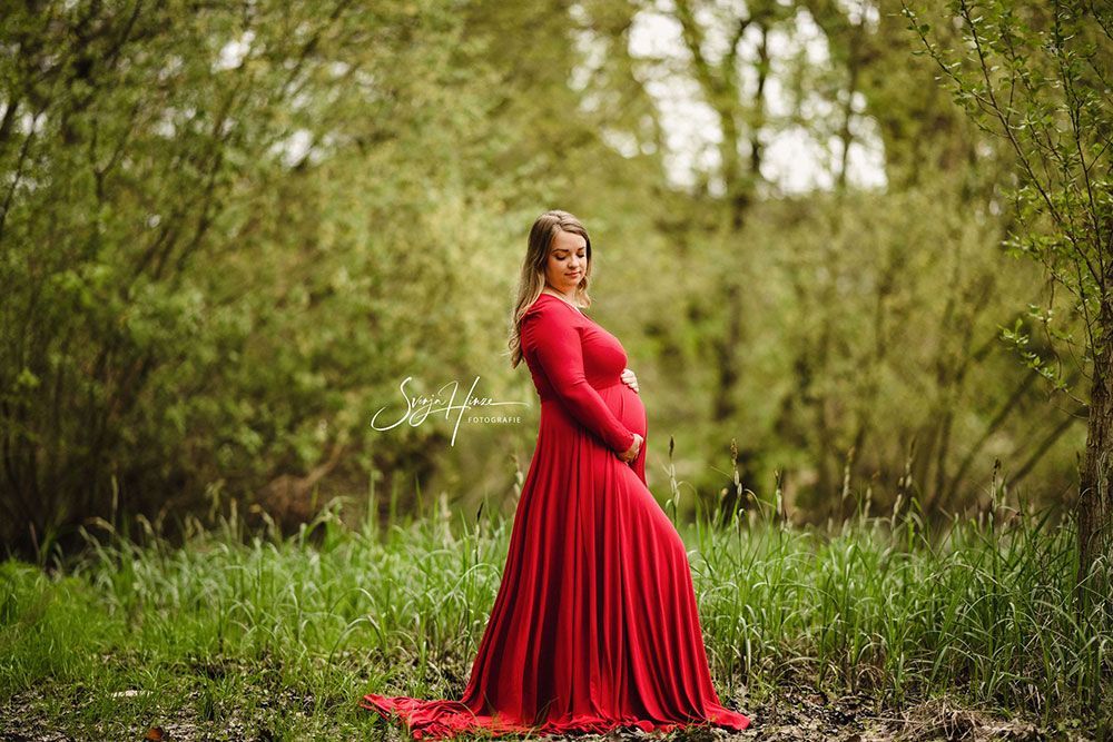 Eine schwangere Frau in einem roten Kleid steht auf einem Feld.