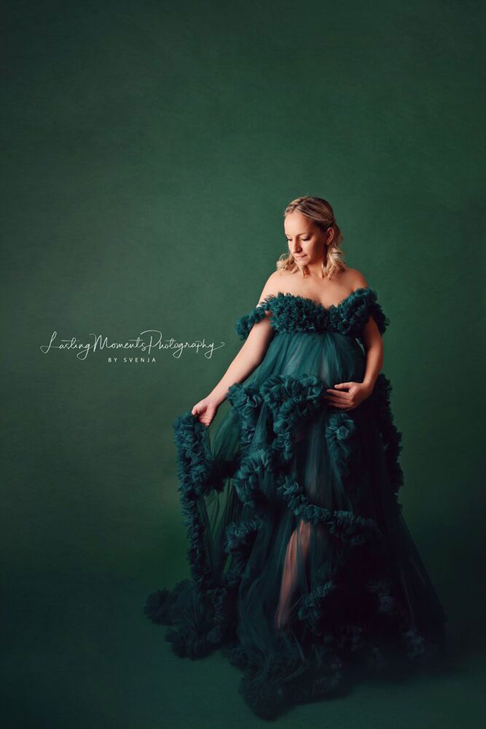 Eine schwangere Frau in einem grünen Kleid steht vor einem grünen Hintergrund.