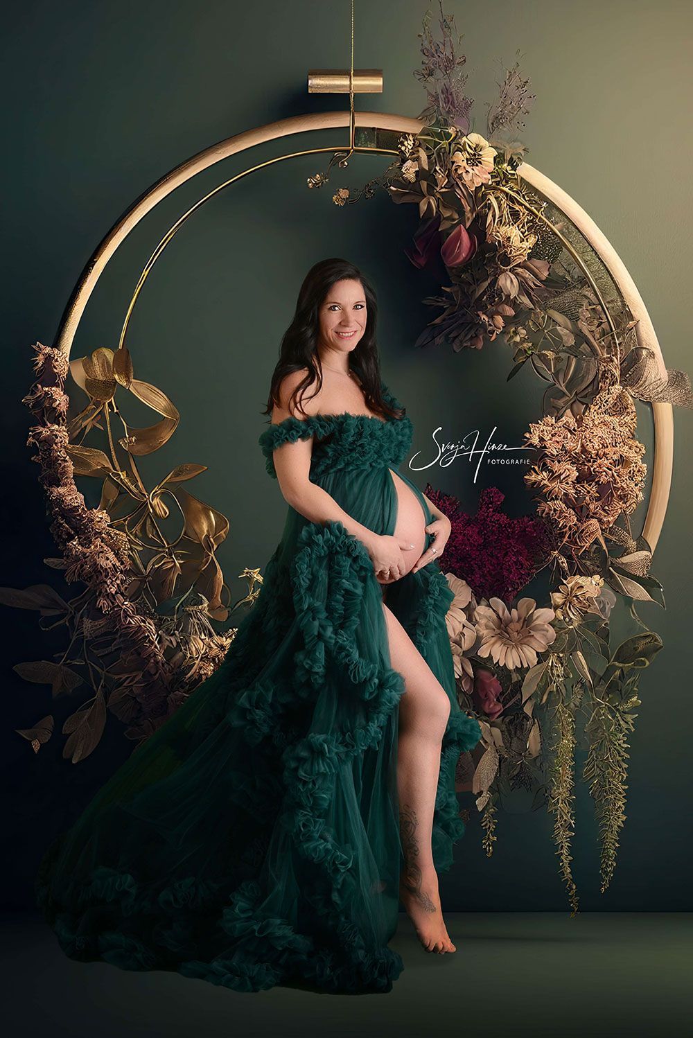 Eine schwangere Frau in einem grünen Kleid steht vor einem Blumenbogen.