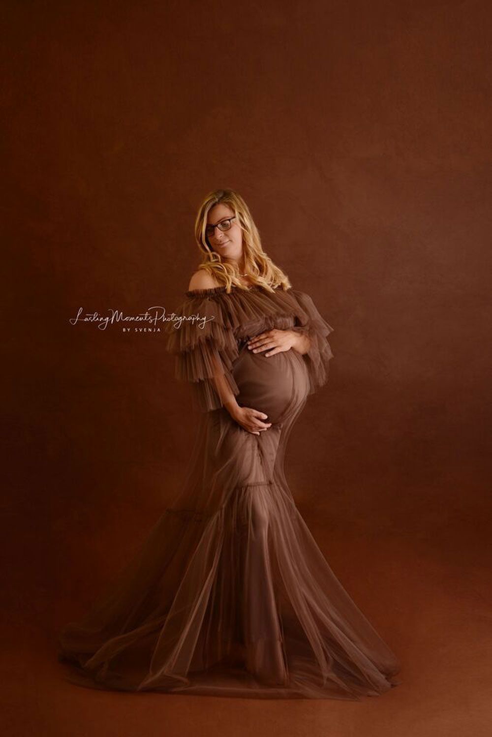 Eine schwangere Frau in einem langen braunen Kleid hält ihren Bauch.