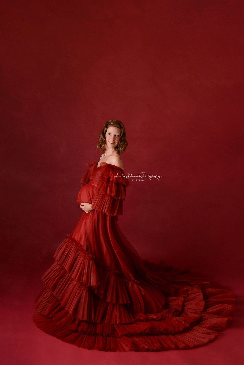 Eine schwangere Frau in einem langen roten Kleid steht vor einem roten Hintergrund.