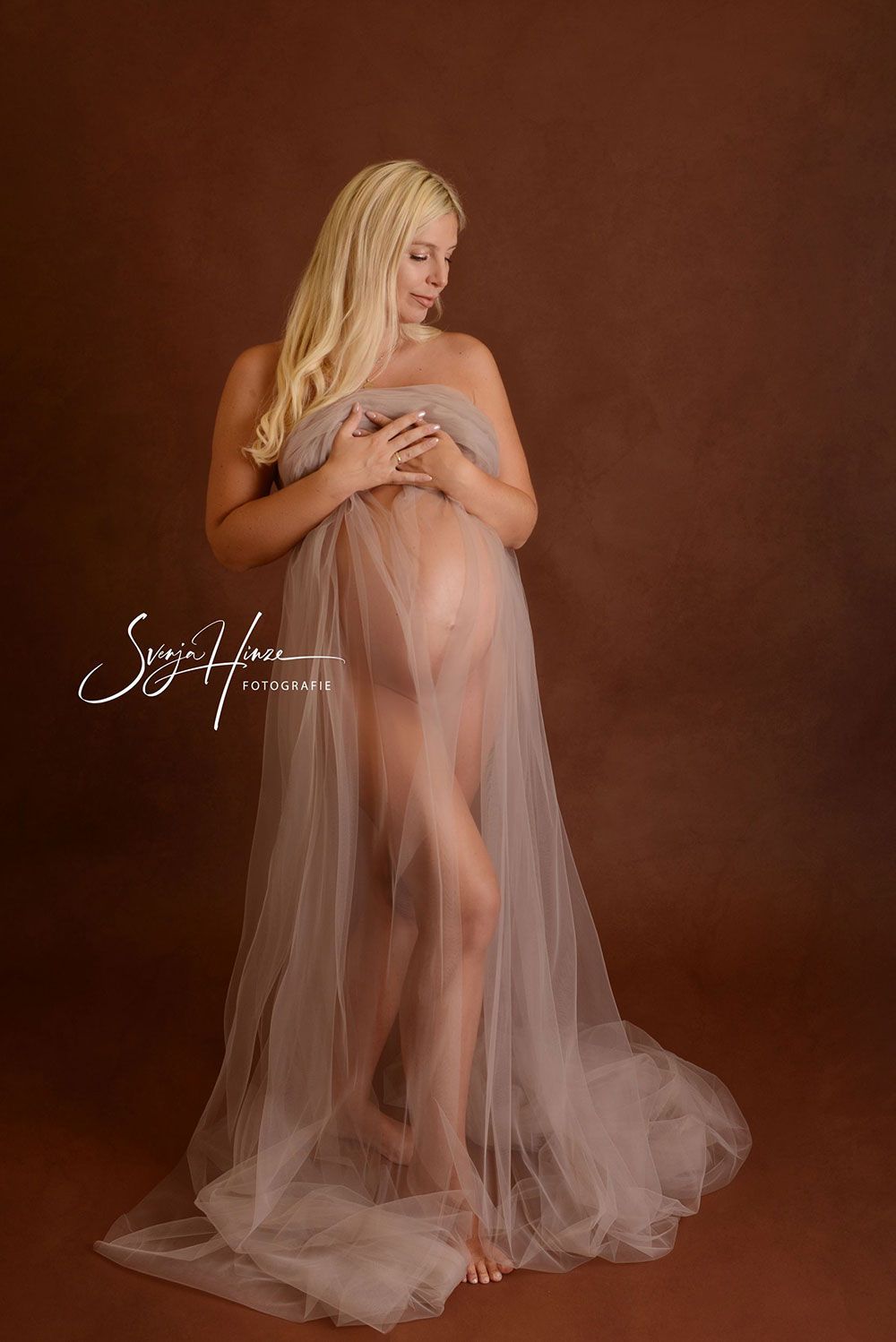 Eine schwangere Frau in einem langen Tüllkleid steht da.