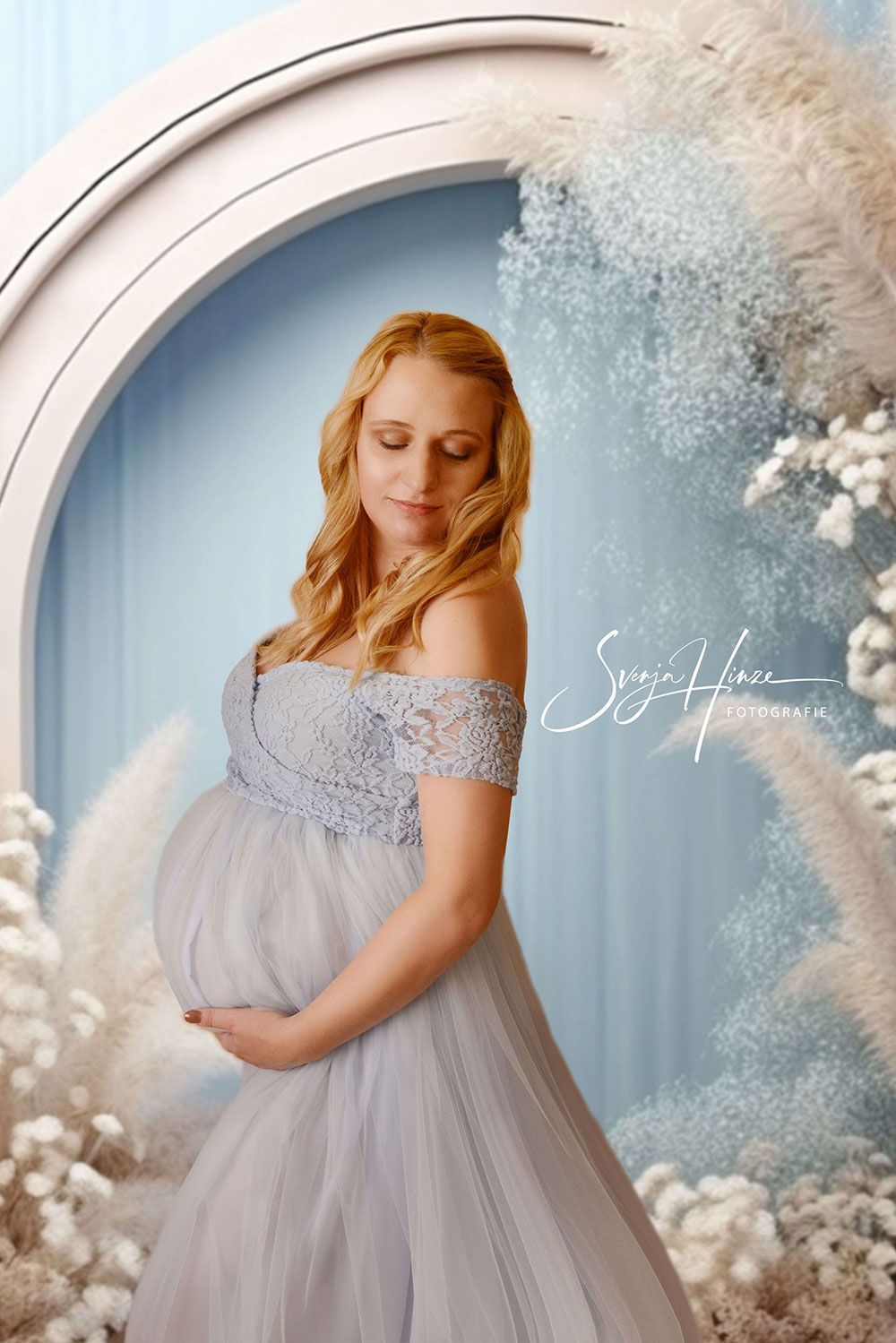 Eine schwangere Frau steht vor einem Fenster und hält ihren Bauch.