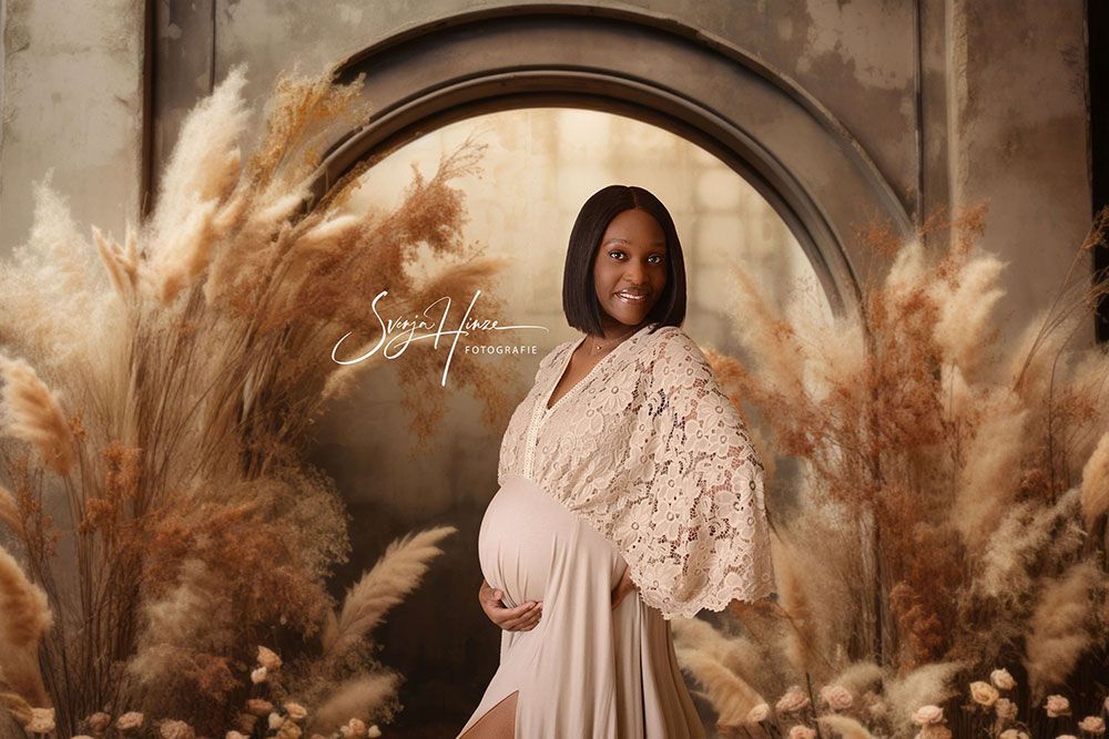 Eine schwangere Frau in einem weißen Kleid steht vor hohem Gras.