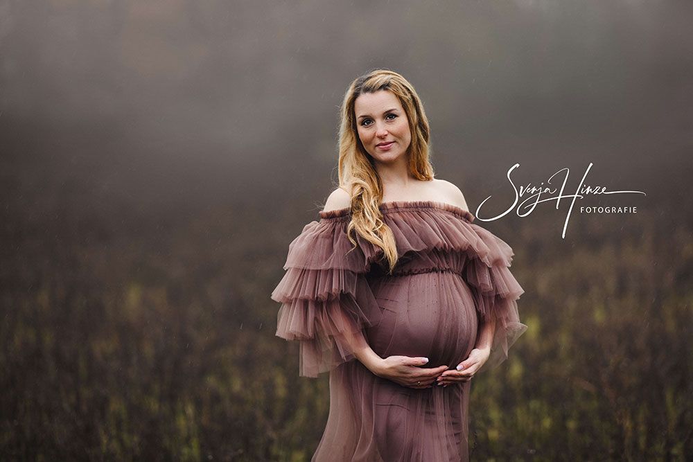 Eine schwangere Frau steht auf einem Feld und hält ihren Bauch.