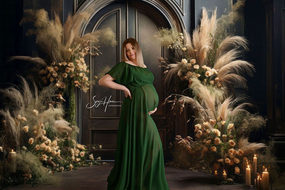 Eine schwangere Frau in einem grünen Kleid steht vor einer Tür, umgeben von Blumen und Kerzen.