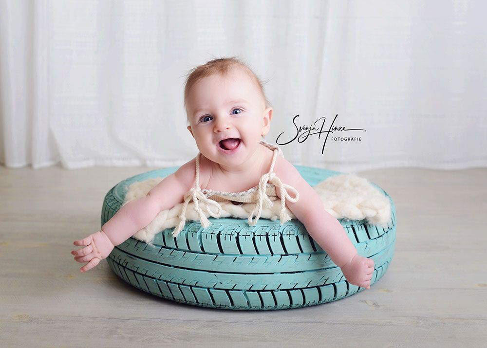 Ein Baby sitzt auf einem Reifen und lächelt.