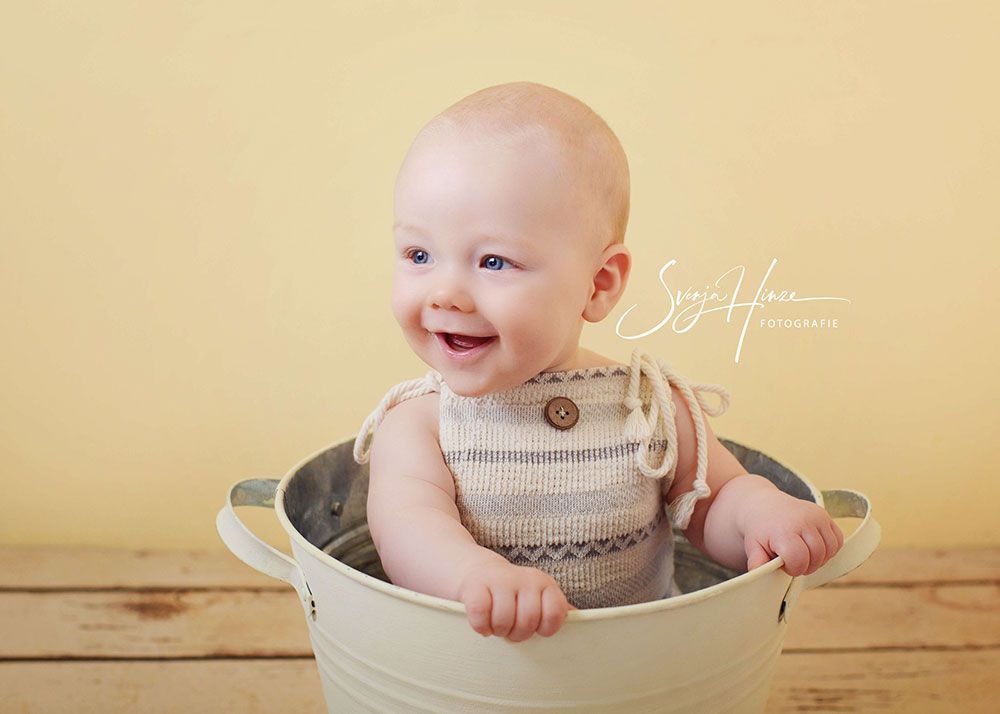 Ein Baby sitzt in einem Eimer Wasser und lächelt.