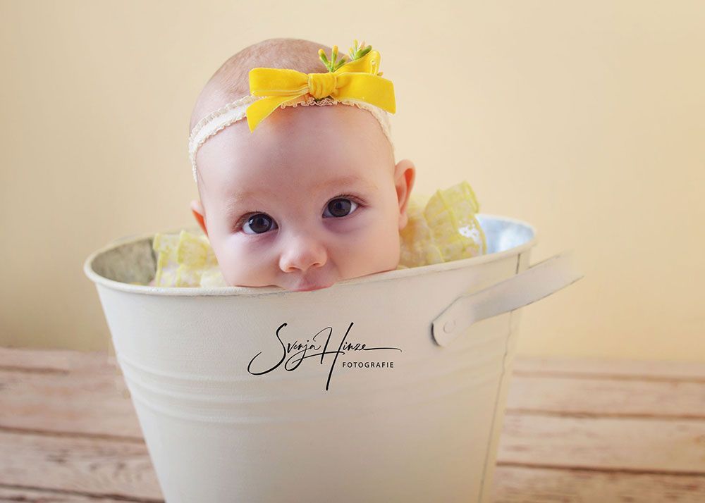 Ein Baby sitzt in einem weißen Eimer auf einem Holztisch.