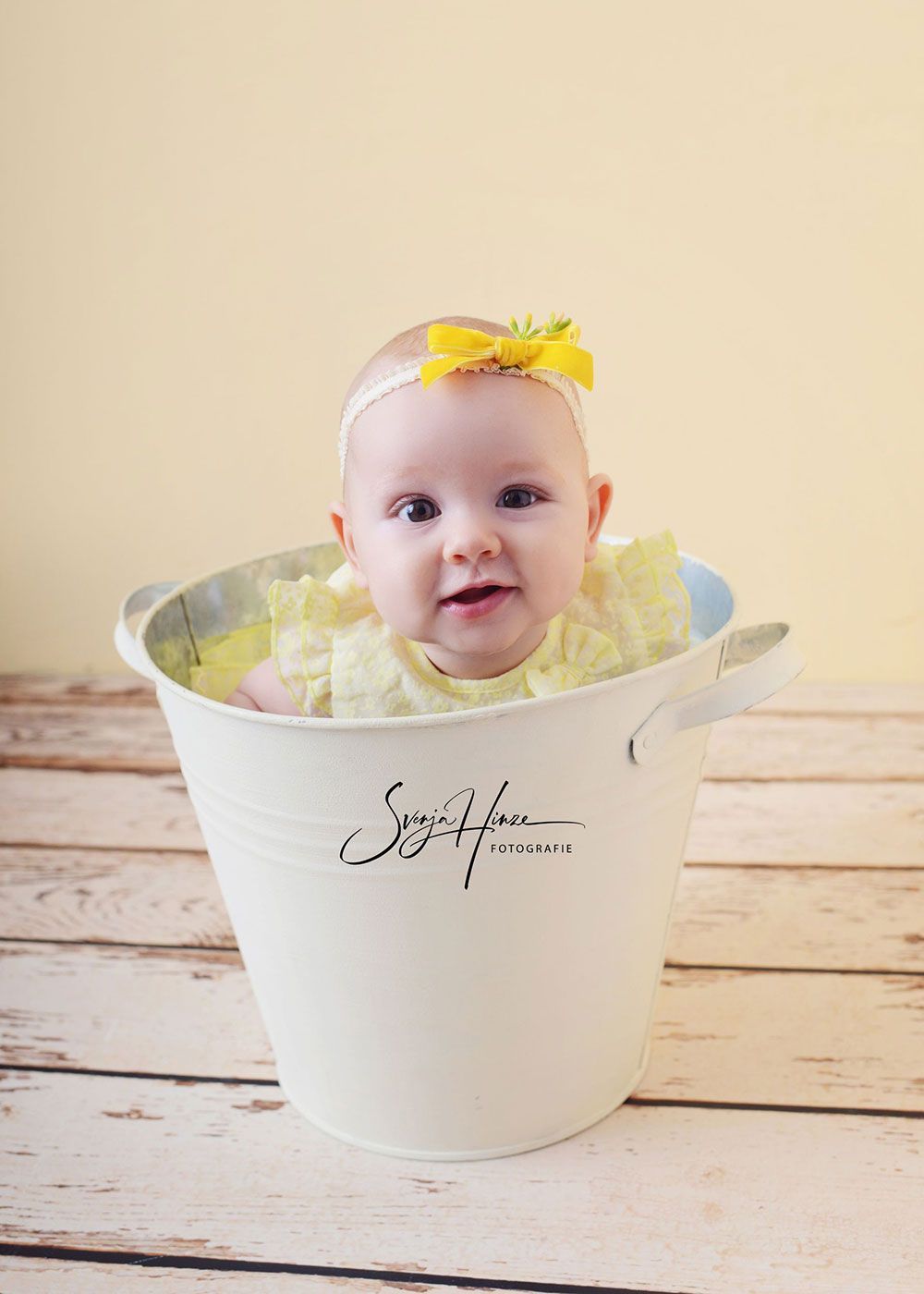Ein Baby sitzt in einem weißen Eimer auf einem Holztisch.