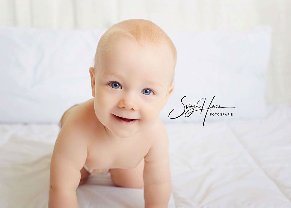 Ein Baby in einer Windel krabbelt auf einem Bett und lächelt.