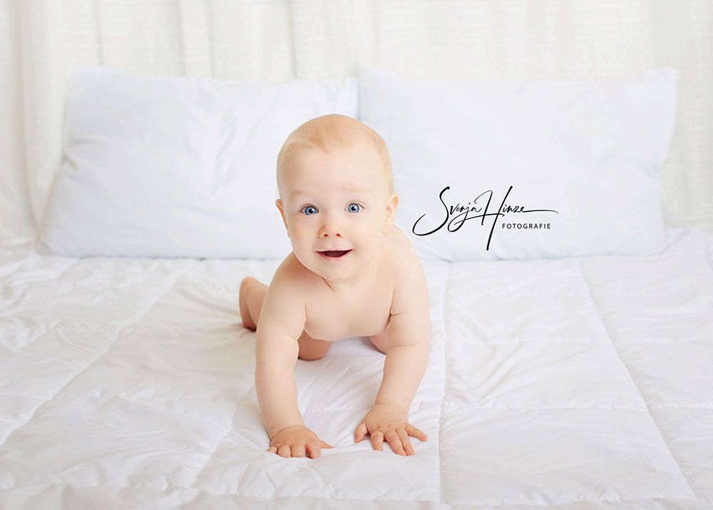 Ein Baby krabbelt auf einer weißen Decke auf einem Bett.