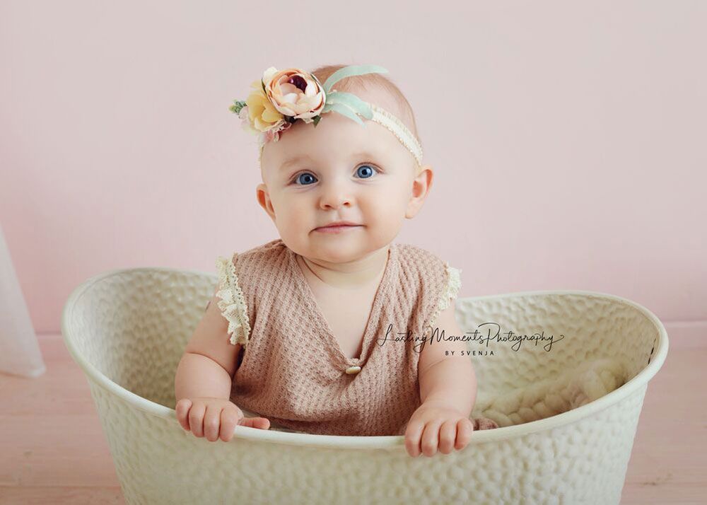 Ein kleines Mädchen mit einem Stirnband sitzt in einem weißen Korb.