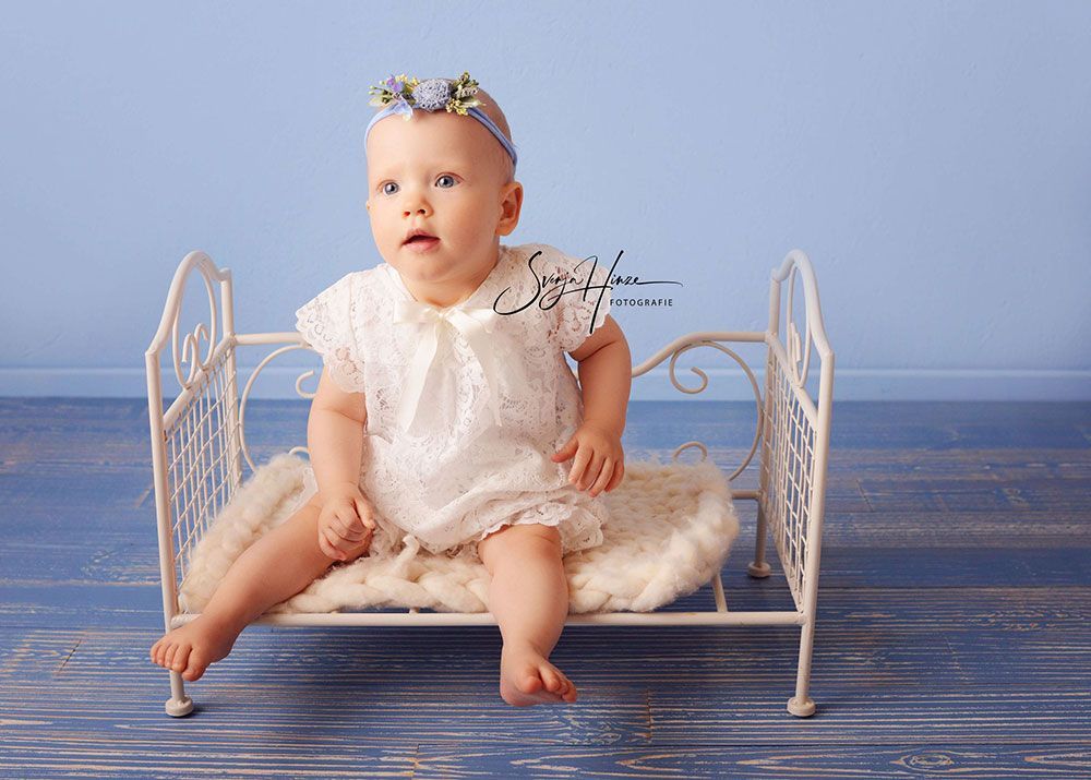 Ein Baby in einem weißen Kleid sitzt in einem weißen Kinderbett.