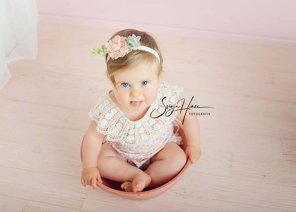 Ein kleines Mädchen sitzt in einer Schüssel auf einem rosa Boden.