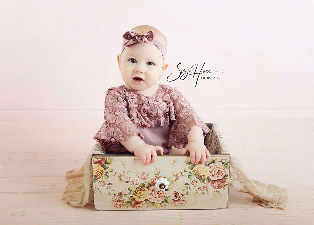 Ein Baby sitzt in einer Schachtel mit Blumen darauf.