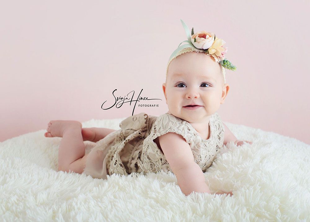 Ein kleines Mädchen liegt auf einer weißen Decke und lächelt.