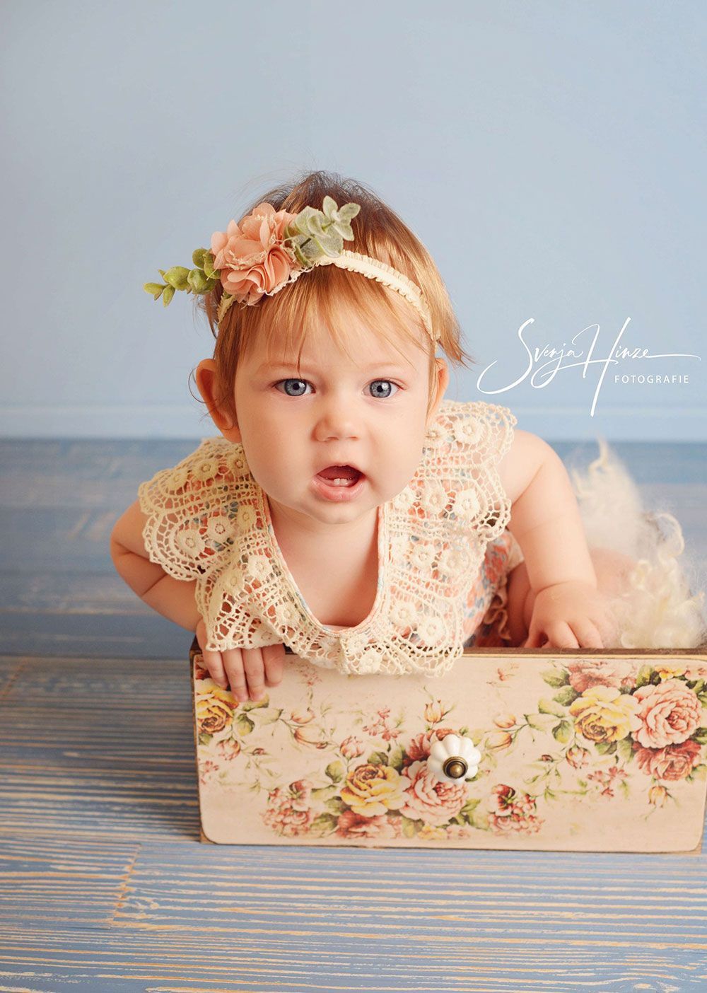 Ein kleines Mädchen krabbelt auf einer Holzkiste.