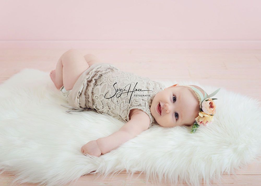 Ein kleines Mädchen liegt auf einem weißen Fellteppich.