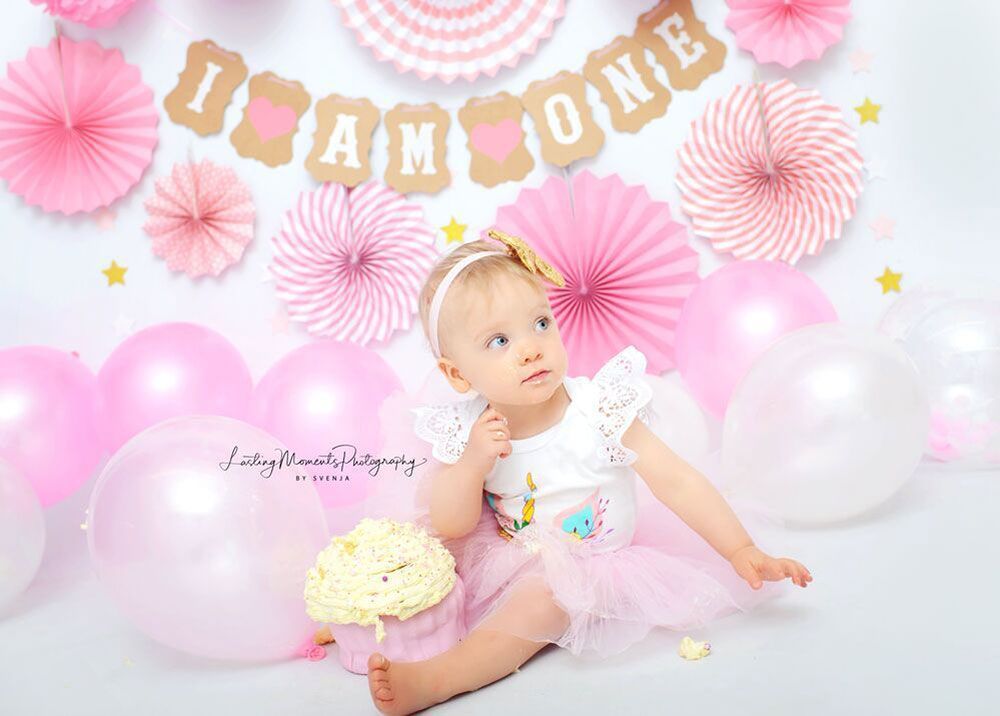 Ein kleines Mädchen sitzt mit einem Kuchen und Luftballons auf dem Boden.