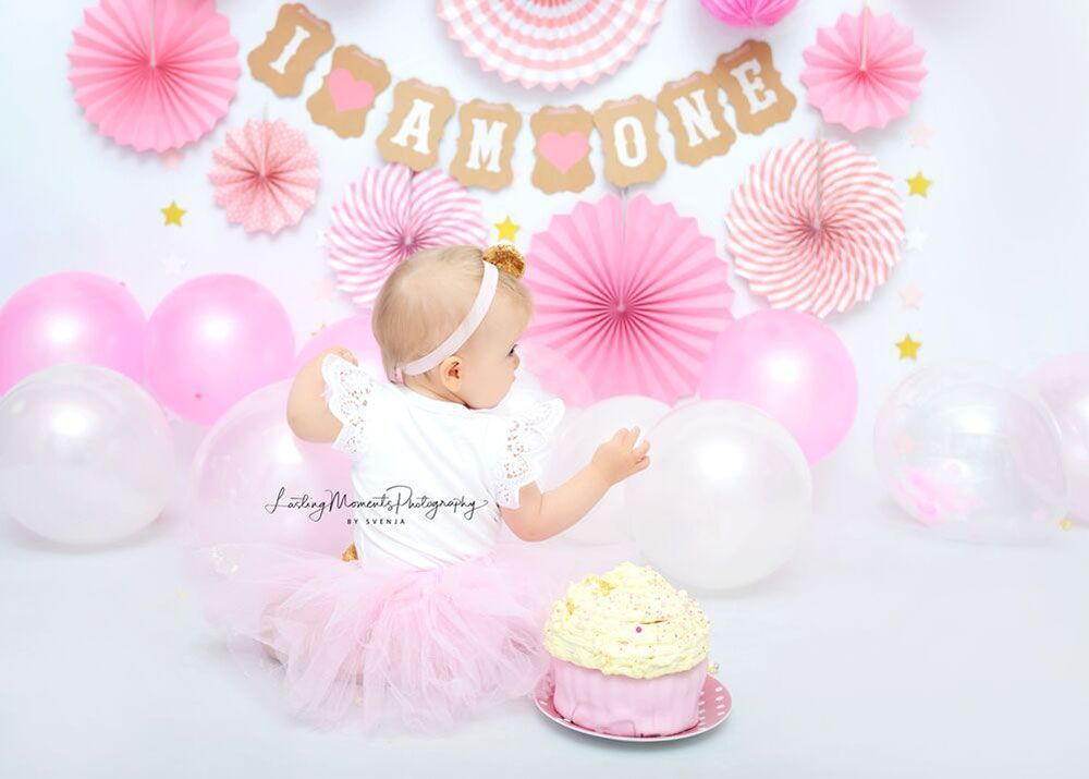 Ein kleines Mädchen sitzt vor einem Kuchen und Luftballons.