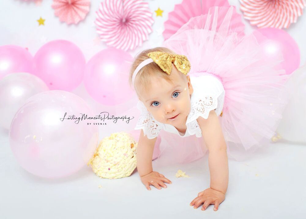 Ein kleines Mädchen krabbelt neben einem Kuchen und Luftballons auf dem Boden.