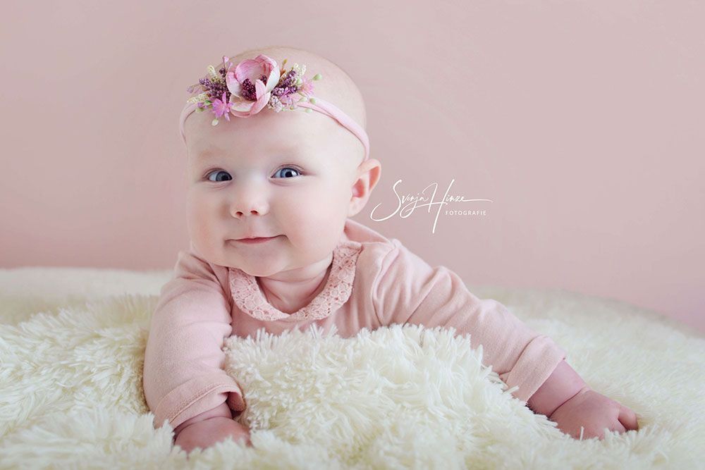 Ein kleines Mädchen mit einem rosa Stirnband liegt auf einer weißen Decke.