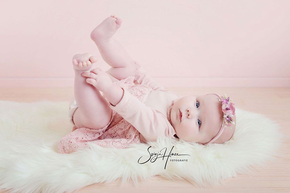 Ein kleines Mädchen liegt auf ihrem Bauch auf einem rosa Teppich.