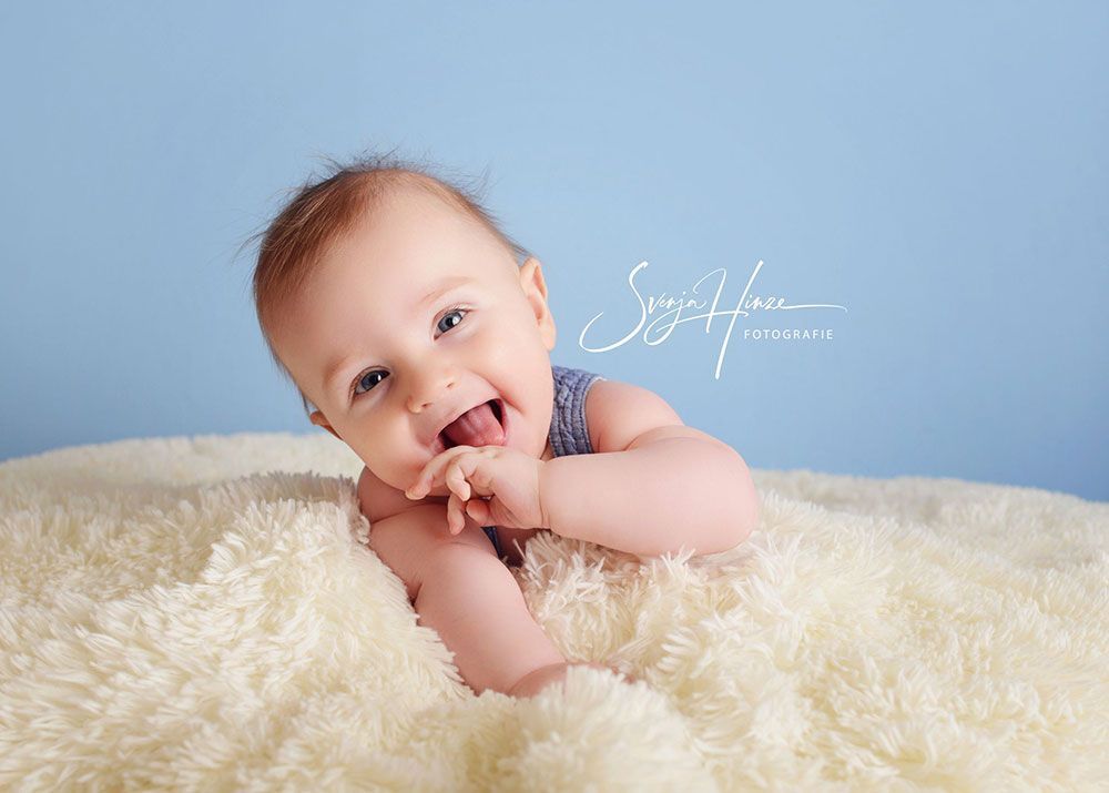 Ein Baby liegt auf einer weißen Decke und lächelt.